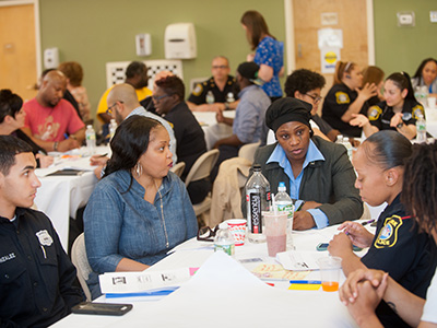 Photo of community members and NPD communicating around tables.